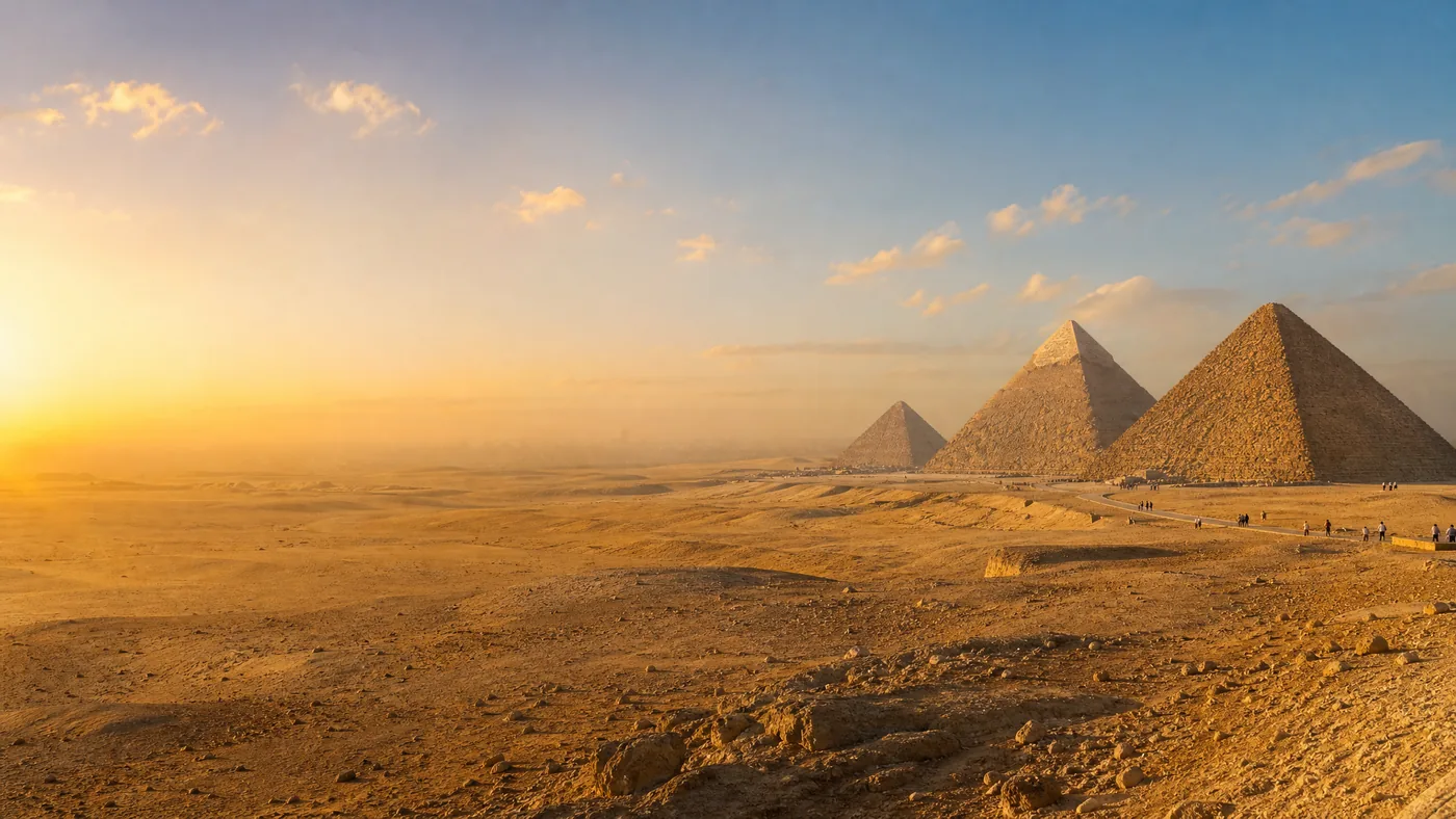 Le tre piramidi di Giza allineate all'ora dorata viste dal lato del deserto, qualche visitatore in lontananza
