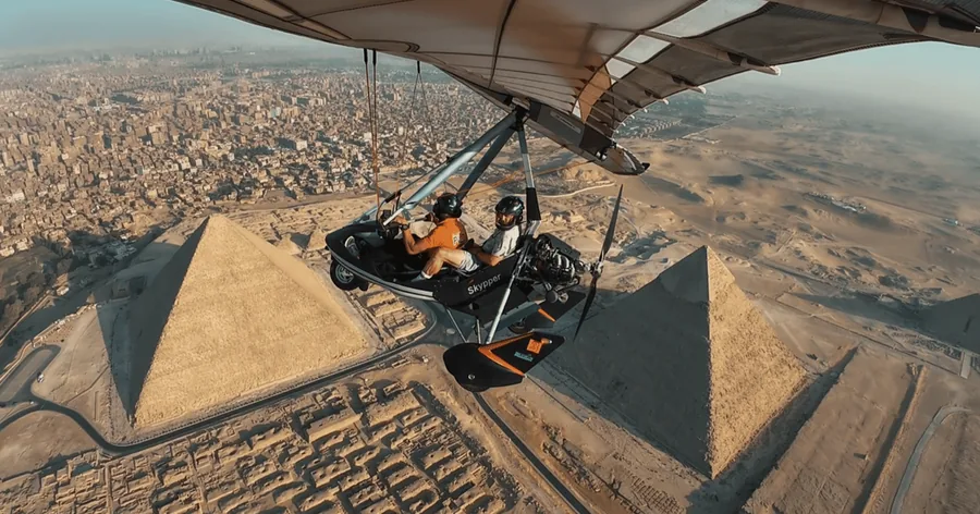 Ein Ultraleichtflugzeug fliegt über den Pyramiden von Gizeh, dahinter erstreckt sich die Stadt Gizeh bis zum Horizont